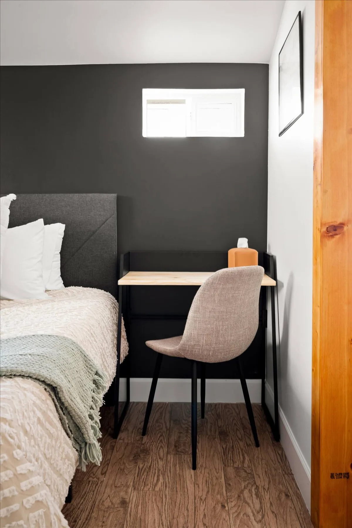 Here, a tranquil bedroom features a small desk with a chair and a decorative item atop it, positioned next to a bed with textured bedding. The setting is peaceful and uncluttered, offering a distraction-free environment that’s perfect for focusing on work or studies.