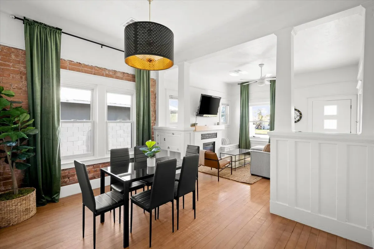 A stylish living area with a dining table and black chairs, green curtains, a fireplace, and a TV mounted on the wall. The arrangement encourages relaxation and social interaction, while the TV setup hints at movie nights and shared entertainment.