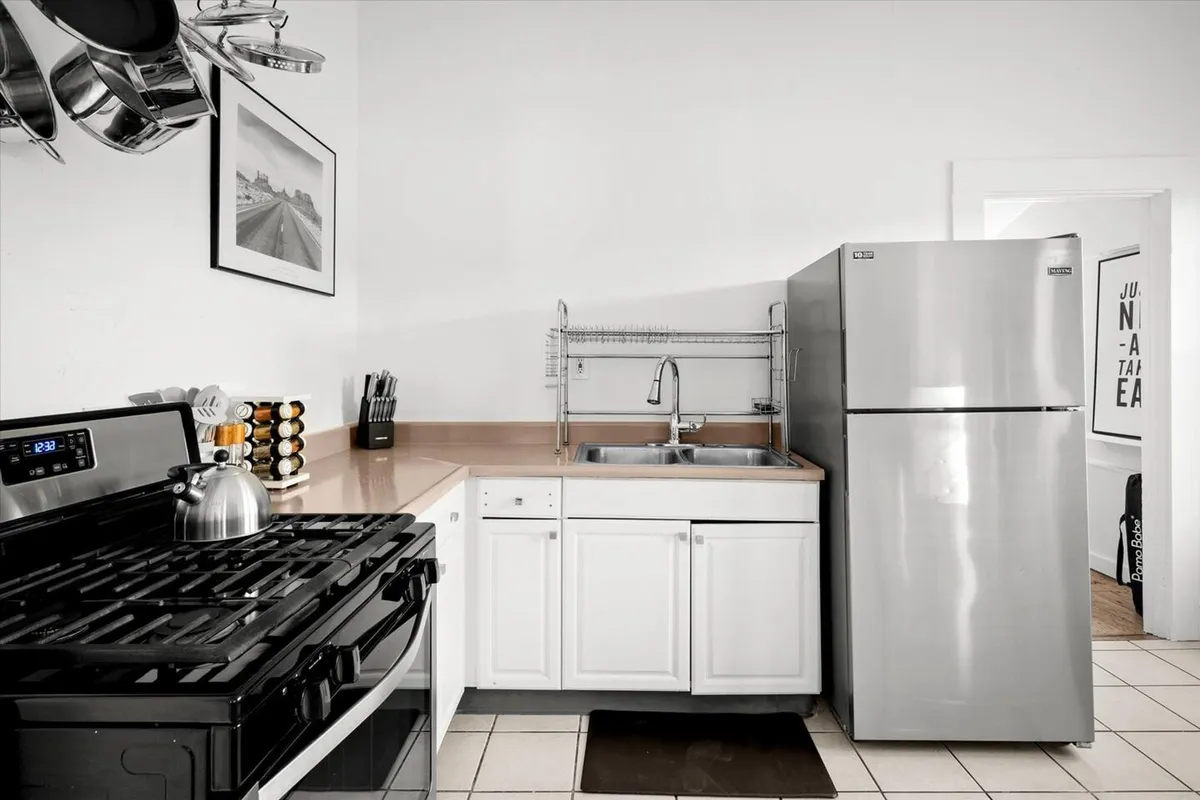 This image features a gas stove, refrigerator, and sink set along a practical kitchen countertop. The workspace is uncluttered and inviting, ideal for everyday meal prep and family cooking. The ambient lighting and modern fixtures give the kitchen a welcoming and efficient vibe.