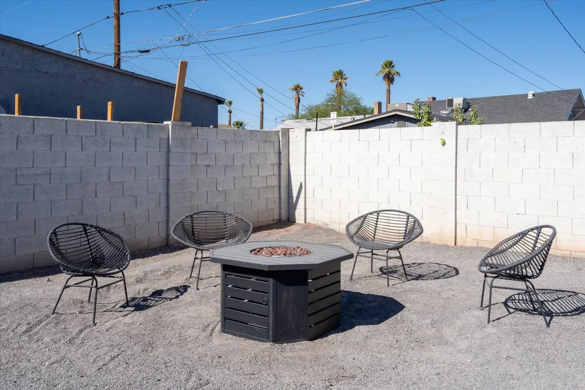A relaxed backyard scene centers on a fire pit with surrounding chairs, creating a natural gathering place for socializing, storytelling, or unwinding under the stars. The space encourages evening relaxation and community connections.