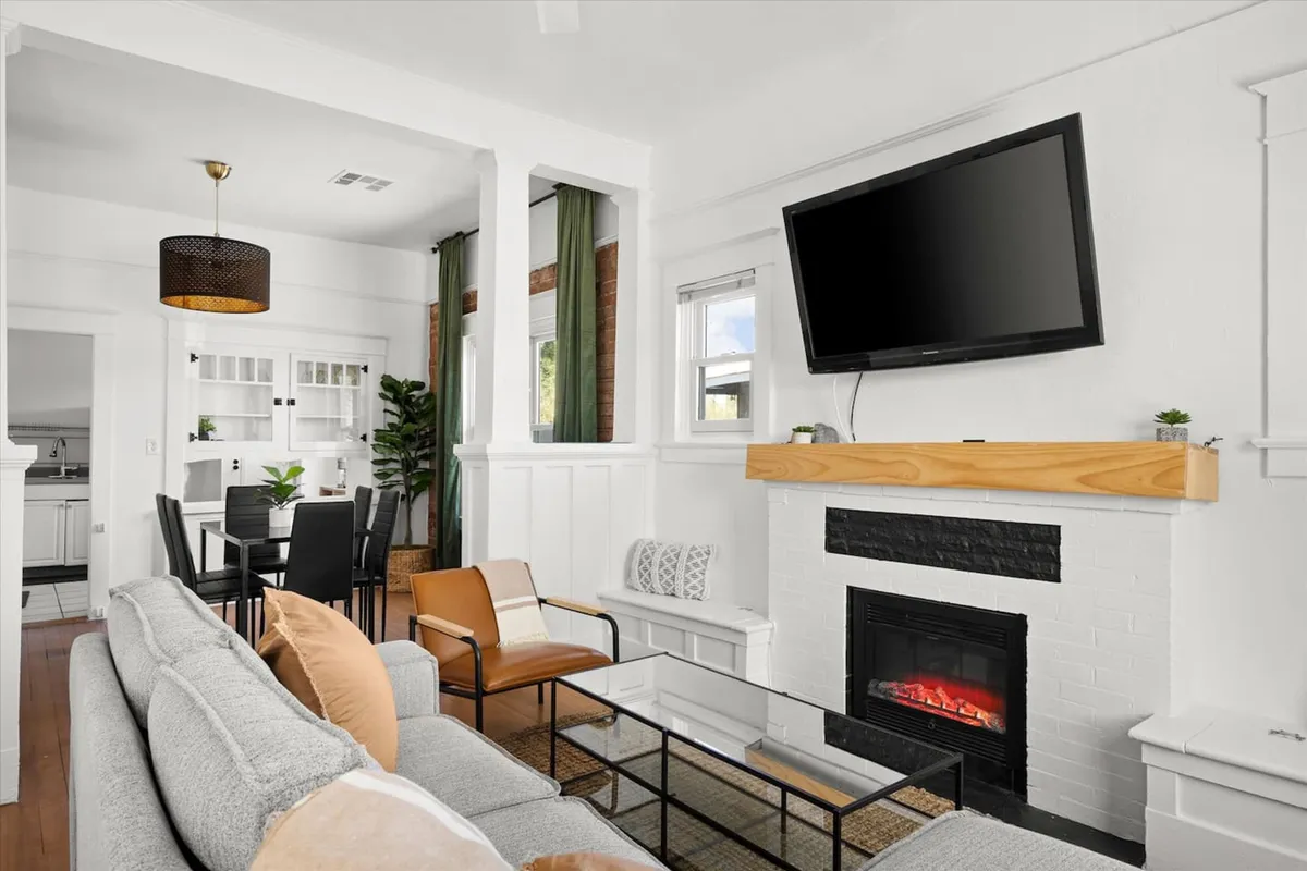 A welcoming living room featuring a plush sofa positioned near a fireplace, an open dining area with green curtains, and a Smart TV. The scene is set for relaxation or entertaining, with comfortable furnishings and cozy lighting contributing to a homey atmosphere.