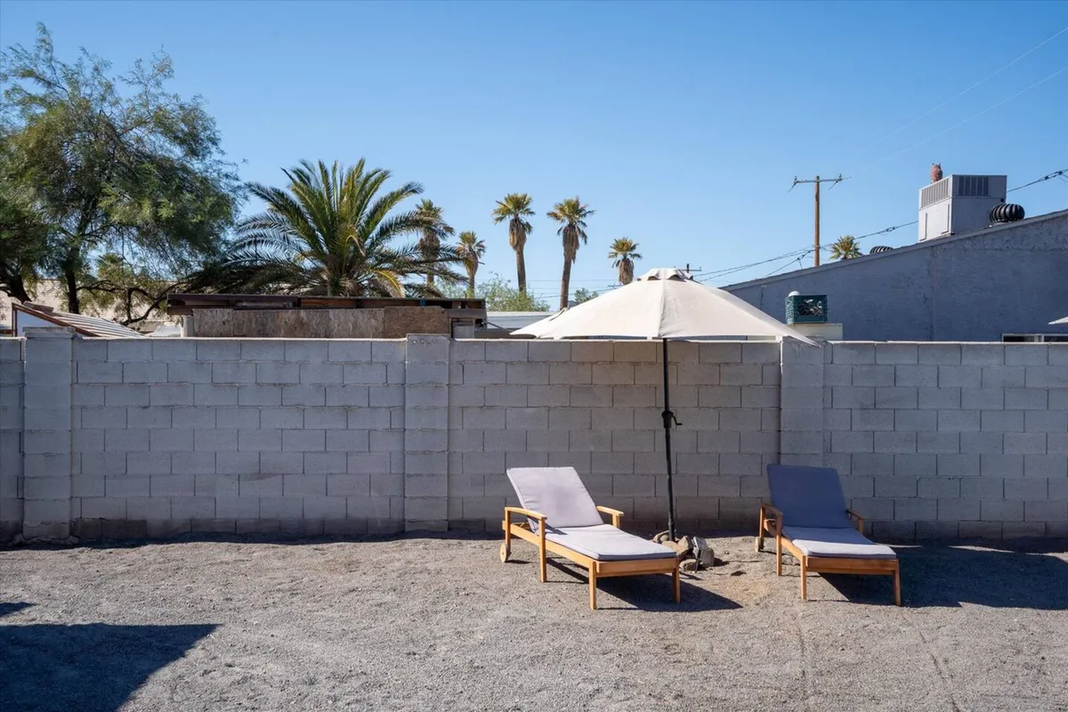 A tranquil patio scene with lounge chairs, a parasol, and palm trees, evoking relaxation and a connection to the outdoors. The setup suggests a peaceful spot for reading, sunbathing, or unwinding as a family.
