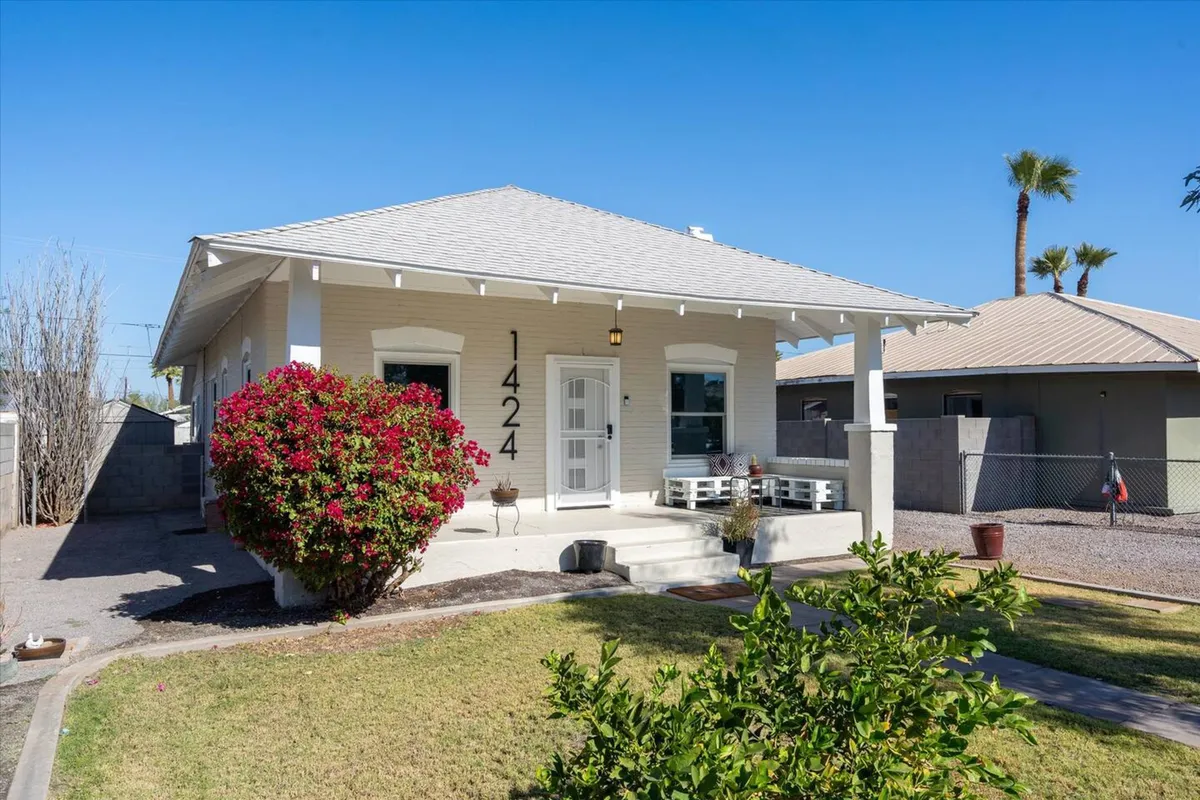 A welcoming front porch is adorned with a flowering bush and the house number 1424 prominently displayed. There's comfortable outdoor seating, perfect for relaxing while soaking up the vibrant Phoenix atmosphere. The porch provides a transitional space between home and neighborhood, inviting residents to engage with their urban surroundings.