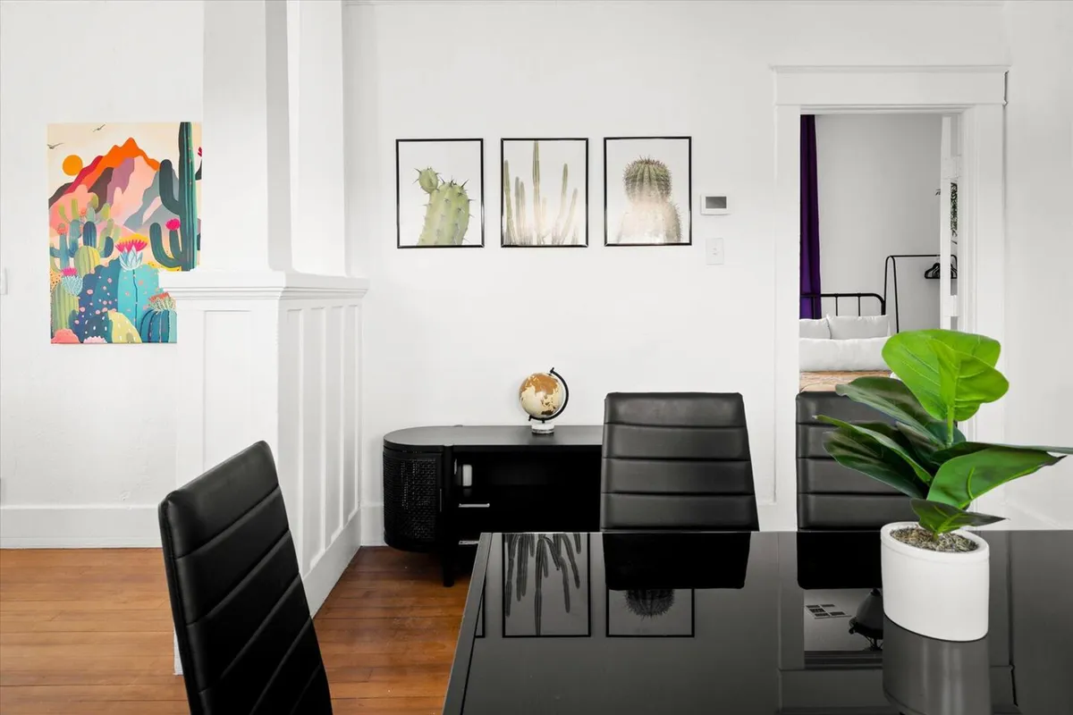 A contemporary, relaxed interior is highlighted by colorful artwork on the wall, framed botanical prints, a globe on the desk, and a green potted plant. The desk space is suitable for work or creative projects, while the surrounding decor inspires creativity and comfort.